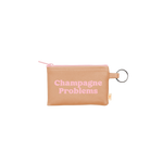 A small zippered pouch with an attached gold key ring. The main color of the pouch is tan and the saying "Champagne problems" is written in pink in the center.