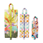 Three rectangular ripstop fabric bags with zippers and top handles displayed vertically side by side. From left to right: the first bag features a vibrant sunrise-inspired design with orange and green rays, clouds, and colorful flowers on a light pink background with a green base and yellow zipper; the middle bag has a pastel wavy check pattern in shades of lavender, mint, peach, and gold with a lavender zipper and handle; the third bag is decorated with a psychedelic multicolored floral print in hues of pi