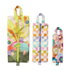 Three rectangular ripstop fabric bags with zippers and top handles displayed vertically side by side. From left to right: the first bag features a vibrant sunrise-inspired design with orange and green rays, clouds, and colorful flowers on a light pink background with a green base and yellow zipper; the middle bag has a pastel wavy check pattern in shades of lavender, mint, peach, and gold with a lavender zipper and handle; the third bag is decorated with a psychedelic multicolored floral print in hues of pi