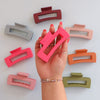 A hand holding a pink claw clip hair accessory. There are a bunch of different colored claw clips that are designed to hold sections of hair in place. 