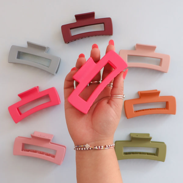 A hand holding a pink claw clip hair accessory. There are a bunch of different colored claw clips that are designed to hold sections of hair in place. 