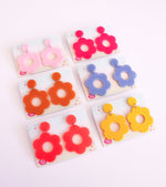 6 bold and playful statement earrings in a retro-inspired daisy flower design. The earrings have a large, acrylic flower with a circular cutout center, hanging from a matching circular stud. The petals are rounded, giving off a fun, 70's style playful vibe!! 