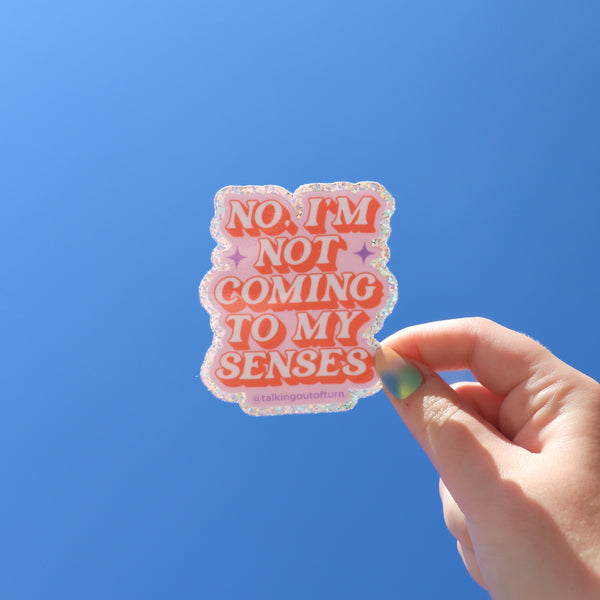 A hand holding a glitter sticker with the saying "No I'm Not Coming To My Senses" written in pink with a coral outline. The word "no"t has two purple diamond s on each side to emphasize the NOT!!