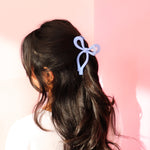 A girl with dark medium length hair wearing an adorable lilac bow clip in the shape of a bow. The bow claw clip is a timeless hair accessory that brightens up any outfit!!