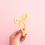 A hand holding a yellow claw clip in the shape of a bow. This yellow bow claw clip in a perfect way to add some cheerfullness to any outfit!!