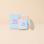 Silly Goose soy candle in clear glass jar with pastel blue label and pink text, displayed with matching gift box on a neutral background. Playful and quirky home fragrance gift.