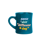 The stylish diner mug features a dark teal background color with the saying "same shit different day" written in light blue, light green, pink, and orange. There is a moon and a sun printed on the mug to represent day and night.