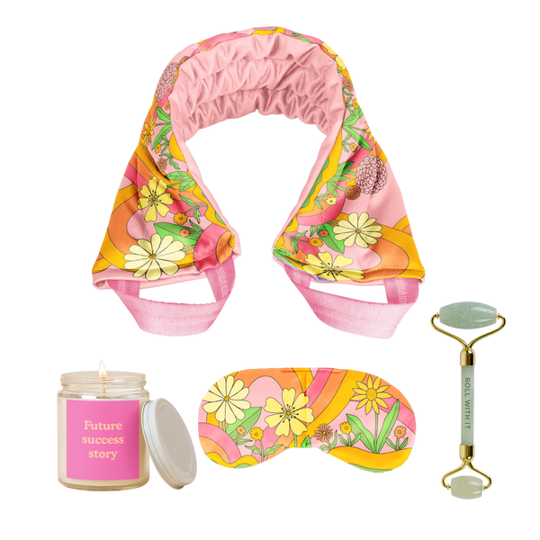 A cute funky set of our self care items that includes a candle with a pink label and a jar lid, a jade green stone face roller with a saying on it, a weighted eye mask in a floral funky daisy print, and a weighted neck wrap in the same print that would be perfect as a gift or for personal self care.