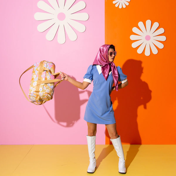 Young lady with sunglasses holding a floral duffle bag.