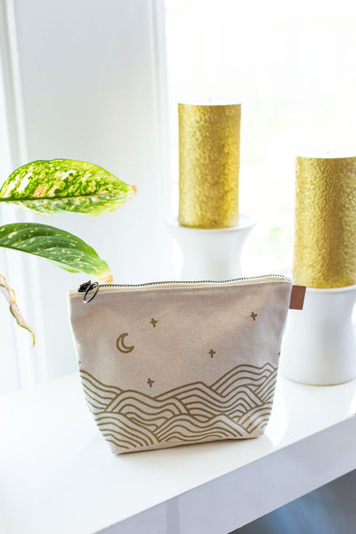 Canvas toiletry bag with leather tab detail and metal zipper, gold wrapped hills with moon and stars