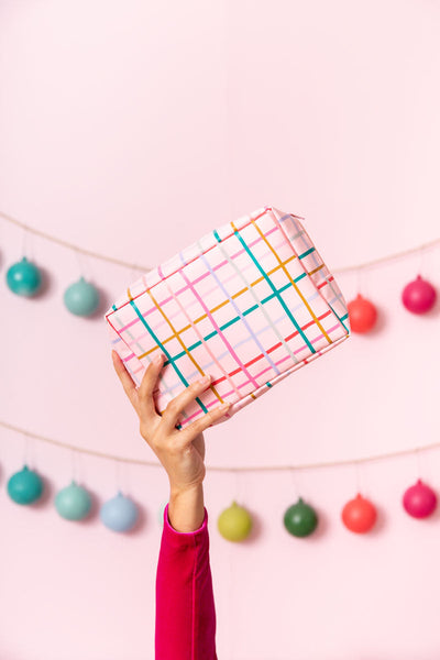 Hand holding up pink, mulit-color plaid pouch in front of garland of ornaments.