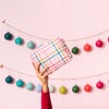 Hand holding up pink, mulit-color plaid pouch in front of garland of ornaments.