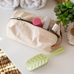 zen ladies doppleganger pouch in tan with a white outline silhouette drawing of a woman's face with blush colored cheeks sitting in a white table with a sage green hairbrush, succulent, white towels and a gold mirror