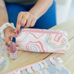 A person closing the Squiggles pouch, which is a long pouch with zipper with squiggly circles all over in pinks, reds, blues, and greens