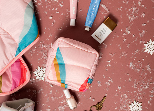 A pink & colorful puffy pouch with snowy confetti and other items around it