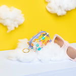 Colorful daisy pattern on a clear vinyl key pouch sitting on a cloud next to sunglasses. 