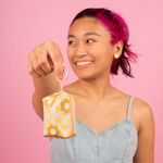 Pink background and a girl holding a light violet and green checker with flowers pattern tag a long key ring