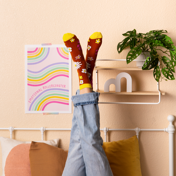 Person wearing "Flower Power" long socks with "Emotional Rollercoaster" print hanging on the wall 