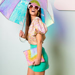 Lady with umbrella holding a puffy rainbow dollface pouch.