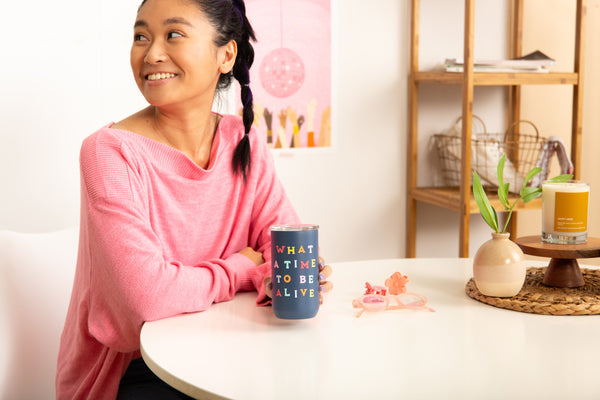 Girl in pink holding a "WHAT A TIME TO BE ALIVE" tumbler