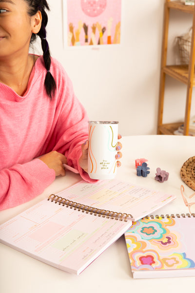 Girl in pink holding an "I'm all over the place" tumbler over a planner