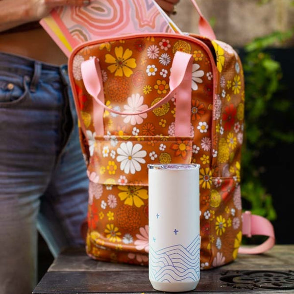 White and blue 16 oz everyday tumbler with Flower Power Backpack in the background and multi-colored journal