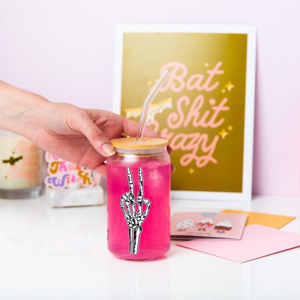 Halloween glass can with lid and a hot pink liquid inside. The design is a skeleton hand giving a peace sign.