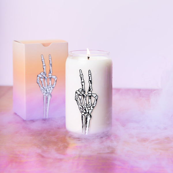 Halloween candle can glass with white skeleton outlined in black making a peace sign 