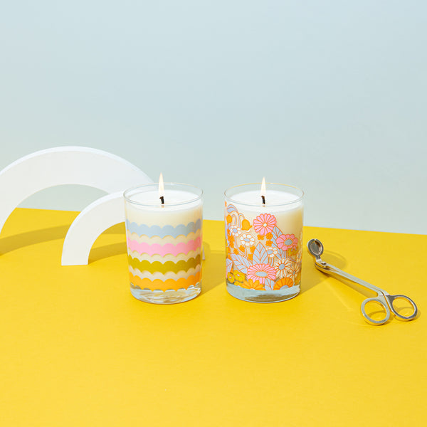 Rising scallops candle rocks glass with gathering flowers pattern candle rocks glass on a mustard yellow surface with misc items.