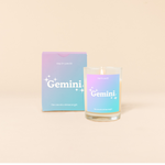 Candle rocks glass with lavender-to-bright blue ombre decal and text that reads "Gemini" with minimalist, white sparkle stars surrounding the text; "the one who shines bright" sits at the bottom of the decal. Box packaging with the same design sits behind glass.
