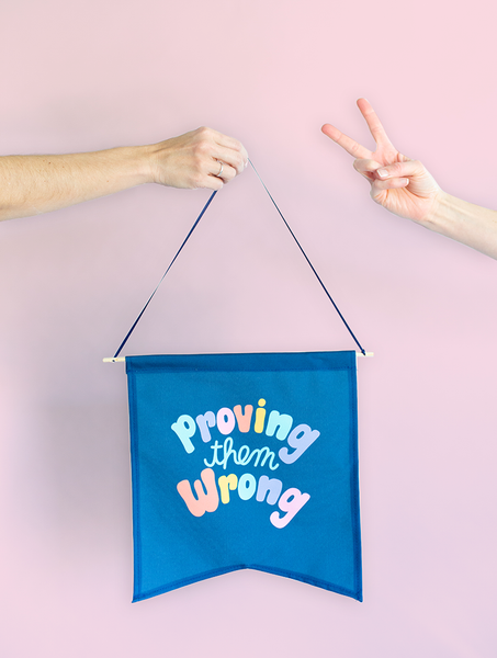 girl holding navy wall pendant saying "proving them wrong" with another girl giving peace fingers