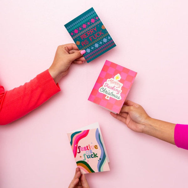 Three hands holding up 3 different Christmas cards.