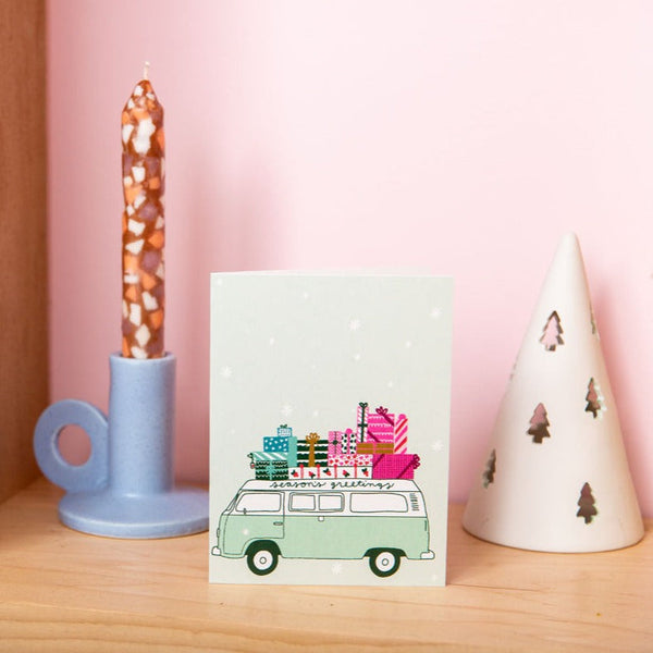 Light green Seasons Greetings van greeting card with seasonal decor behind it