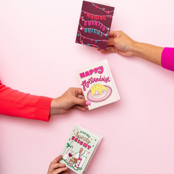 Three hands holding up three different holiday cards. 
