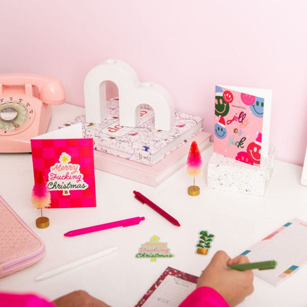 A white desk featuring many seasonal items with someone writing down with a green pen
