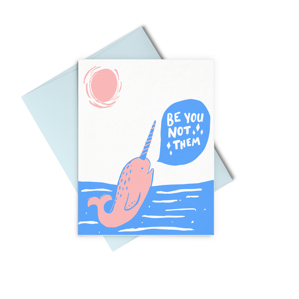 Letterpress greeting card showing a cute pink narwhal with a blue and pink horn rising out of the ocean to say Be You Not Them in a speech bubble
