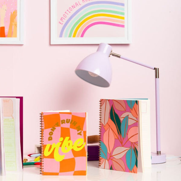 Small don't ruin my vibe goal getter and a large radiance floral goal getter undated planners around by wall art, and light purple lamp.