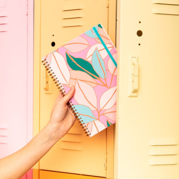 a hand putting a small pink goal getter with multicolor pastel leaves and a blue elastic band in a locker.