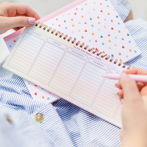 On the Horizon Weekly Deskpad laying on top of a Tiny Hearts Notebook. 