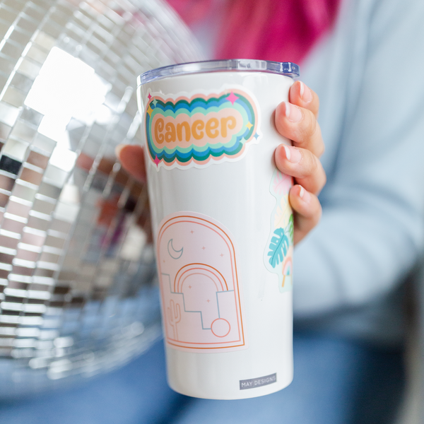 Lady holding a white tumbler with a colorful "cancer" astrology sticker on the side.