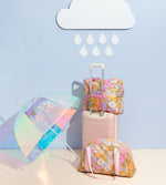 Floral patterned stowaway bag sitting on top of luggage with an umbrella next to it.