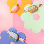 All small multi-color puffy bag on colorful daisy displays. Pink background.