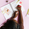 a girl writing in a notebook with a a cute bright pink sticker that says wild child on top