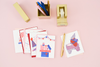 A collection of birthday cards. The two cards are as follows from left to right: A white card with a multi colored pile of birthday presents and a banner across the top. A white card with a light pink, medium pink and red unicorn pinata. There is a gold desk set above the cards.
