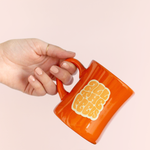 girl holding a tilted orange old fashioned diner-style mug with saying "all the feels" in lighter orange with yellow shadow.