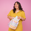 Girl holding a colorful checkers pattern mini backpack. Pink background.