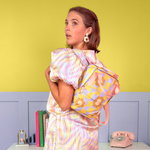 Girl wearing a cool funky daisy pattern mini backpack. Citron/periwinkle background with misc items on a table.