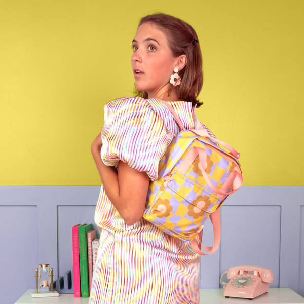 Girl wearing a cool funky daisy pattern mini backpack. Citron/periwinkle background with misc items on a table.