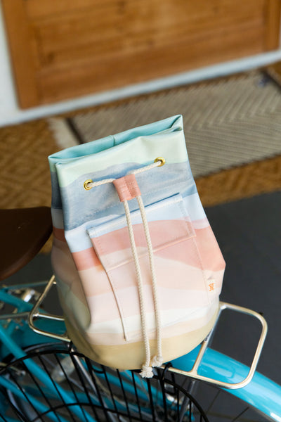 A bucket bag with multicolored pastel diagonal stripes sitting on a bike bracket.