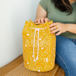 Woman in olive green shirt and jeans sitting next to a golden yellow bucket bag zen ladies talking out of turn